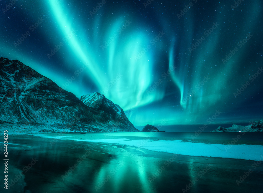 Amazing aurora borealis. Northern lights in Lofoten islands, Norway. Starry sky with polar lights. Night winter landscape with aurora, sea with frosty coast and sky reflection, snowy mountains. Travel