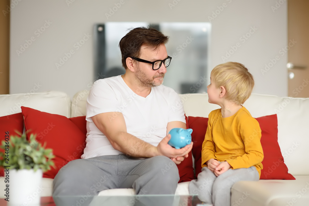 Father and son putting coin into piggy bank Father and son putting coin into piggy bank