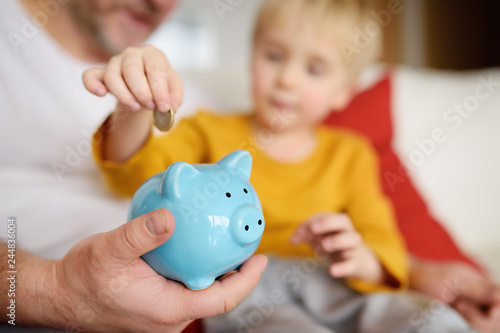Foto Father and son putting coin into piggy bank