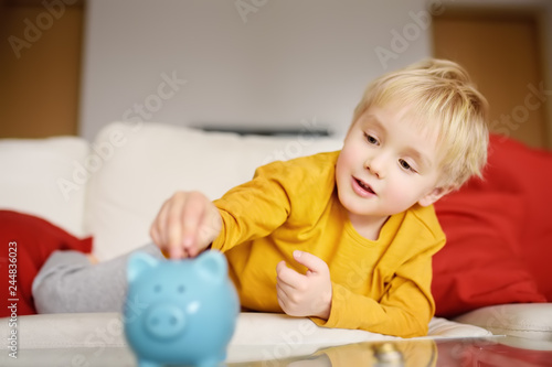Little boy putting coin into piggy bank