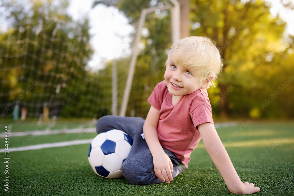 Little boy having fun playing a soccer/football game on summer day. Active outdoors game/sport for children. Little boy having fun playing a soccer/football game on summer day. Active outdoors game/sport for children.