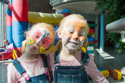 two little girls with brightly decorated faces of a butterfly and a lion cub, having fun at a children's party