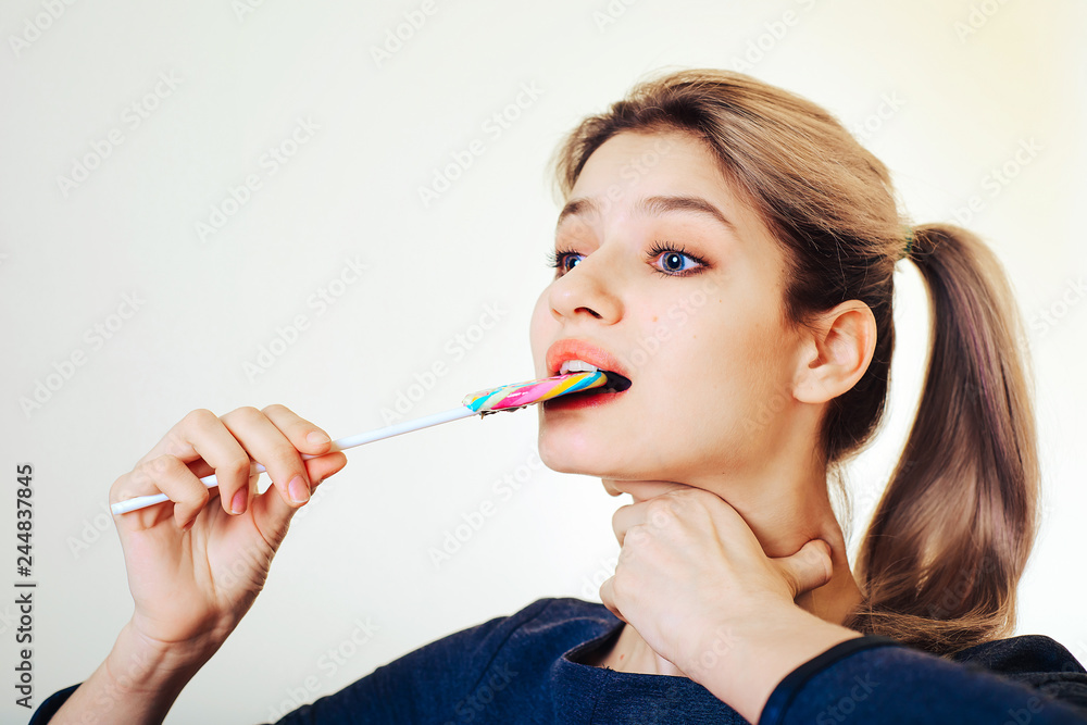 A beautiful young girl bites a candy candy, holds her throat with her other hand. The concept of greed, the restriction of the use of sweet. A beautiful young girl bites a candy candy, holds her throat with her other hand. The concept of greed, the restriction of the use of sweet.