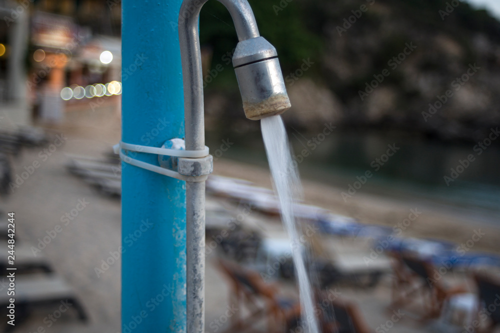 Water Pouring from Shower Head. Public Shower for Outdoor swimming under the Blue Cloudy Sky. Closeup Angle Shot of Pipe Tied to Pole by Plastic Strip Seal Water Pouring from Shower Head. Public Shower for Outdoor swimming under the Blue Cloudy Sky. Closeup Angle Shot of Pipe Tied to Pole by Plastic Strip Seal