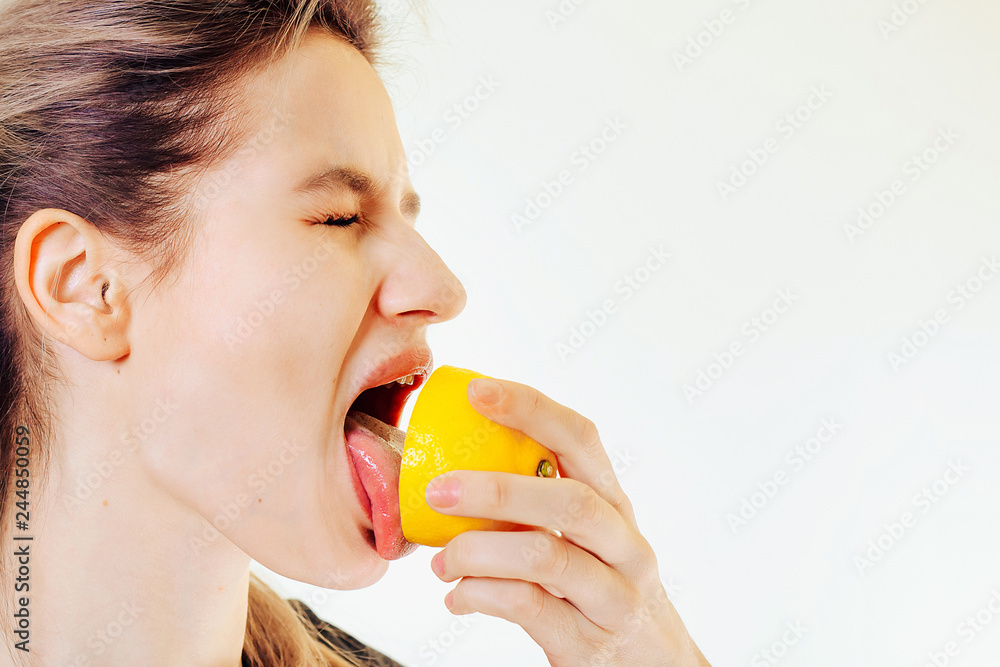 An attractive girl holds a lemon in her hand and licks it with a squint of sour taste. An attractive girl holds a lemon in her hand and licks it with a squint of sour taste.
