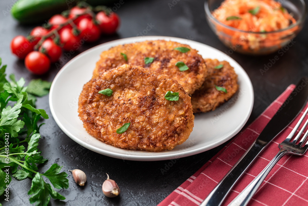 Cutlets lie on a white plate. Chicken cutlets lie among the vegetables on a black stone table. Cutlets lie on a white plate. Chicken cutlets lie among the vegetables on a black stone table.