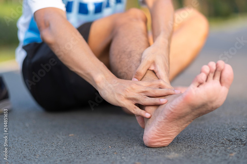 Young fitness man holding his sports leg injury. muscle painful during training. Asian runner having ankle ache and problem after running and exercise outside morning. sport and healthy concepts