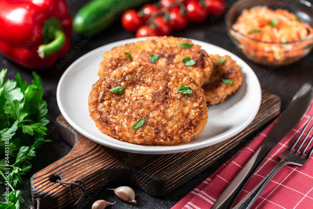 Cutlets lie on a white plate. Chicken cutlets lie among the vegetables on a black stone table.