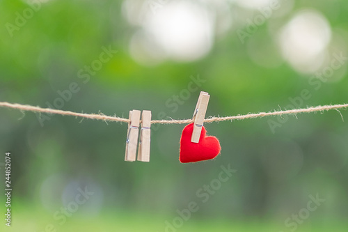 Red heart shape decoration hanging on line with copy space for text on green nature background. Love, Wedding Romantic and Happy Valentine’ s day holiday concept