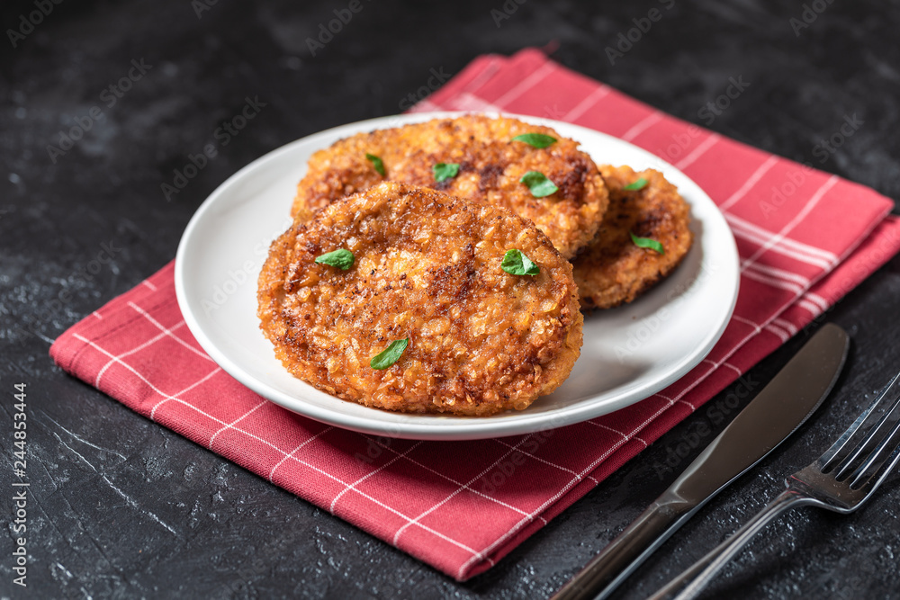 Cutlets lie on a white plate. Chicken cutlets lie among the vegetables on a black stone table. Cutlets lie on a white plate. Chicken cutlets lie among the vegetables on a black stone table.