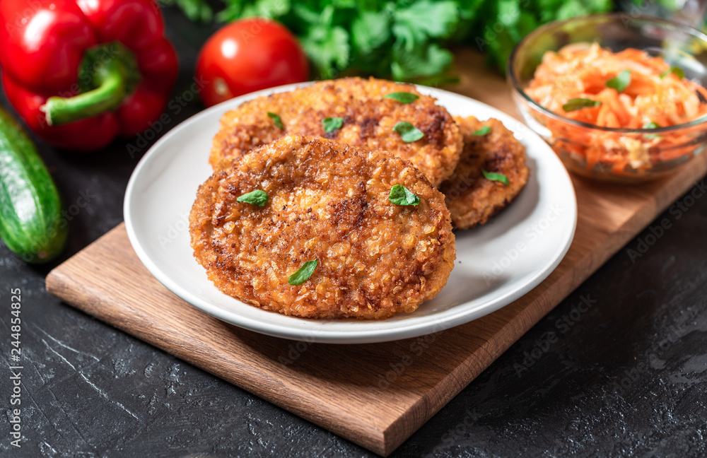 Cutlets lie on a white plate. Chicken cutlets lie among the vegetables on a black stone table.