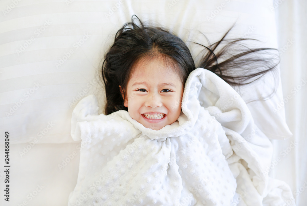 Happy little girl lying on bed with blanket and looking at camera. Top view. Happy little girl lying on bed with blanket and looking at camera. Top view.