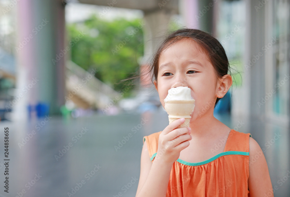 Smiling little Asian kid girl enjoy eating ice cream cone Smiling little Asian kid girl enjoy eating ice cream cone