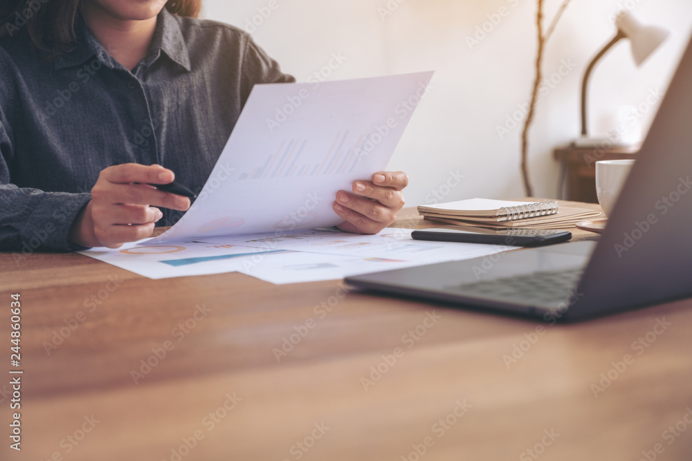 A businesswoman writing and working on business data and document with laptop on the table in office A businesswoman writing and working on business data and document with laptop on the table in office