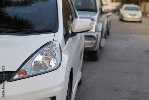 Closeup of front side of white car and other cars parking beside the street. © Amphon