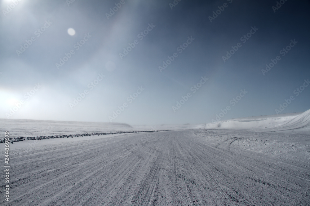 Fototapeta premium An ice road leading towards snow covered hills with a partial sundog located near the community of Cambridge Bay, Nunavut, Canada