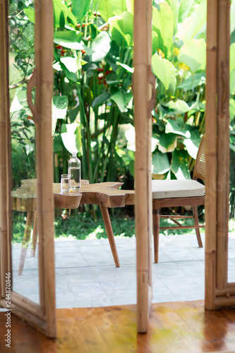 Table from tree stump with glass bottle of water standing it home terrace. Unmanufactured and cracked wood massif of the table. Artistic processing of wood. Loft furniture. Modern furnishings.