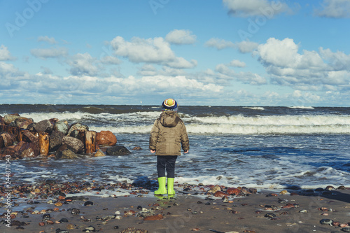 child in rubber boots on the shore of the cold Baltic Sea photo