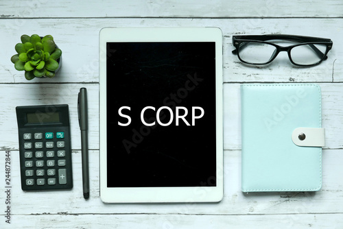 Business concept. Top view of plant,calculator,glasses,pen,notebook and tablet written with S Corp on white wooden background. photo