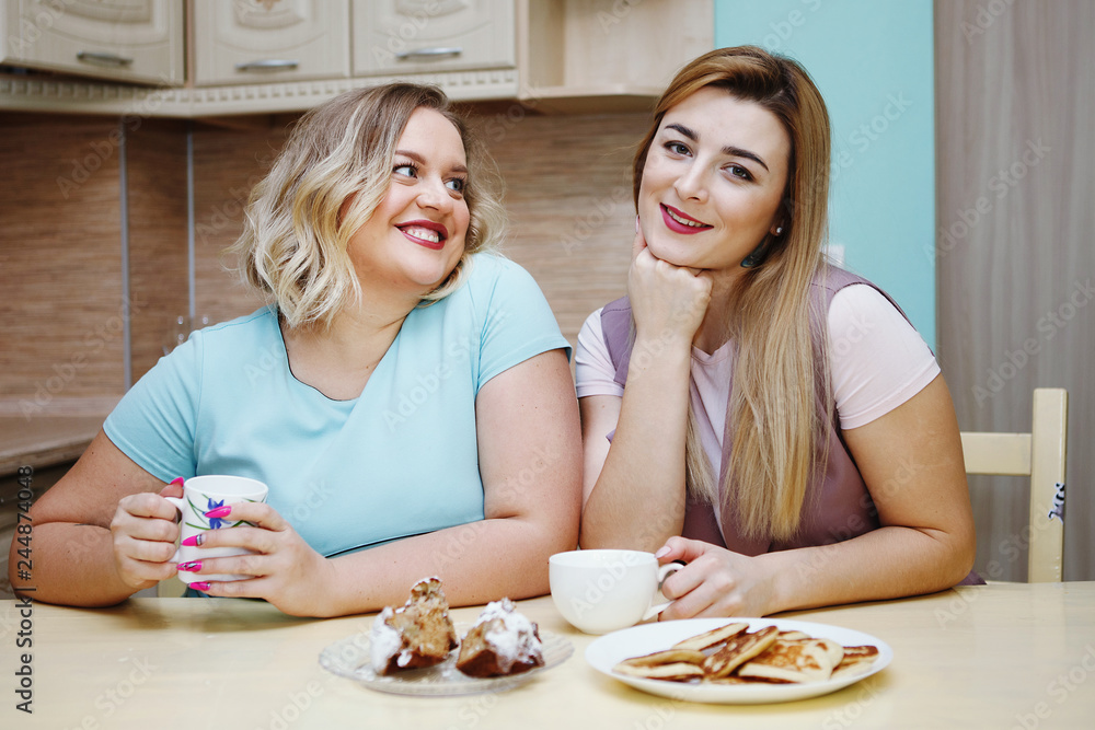 Two girlfriends women in the kitchen are having fun and eating food. Two girlfriends women in the kitchen are having fun and eating food.