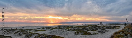 Coronado Beach in San Diego by the Historic Hotel del Coronado, at sunset with unique beach sand dunes, panorama view of the Pacific Ocean, silhouettes of people walking and boats in California, Unite