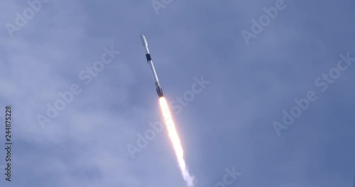 Rocket launching into space through blue skies and clouds. Flames and smoke trail behind the rocket. 4K video at 120 fps slow motion. With audio. photo