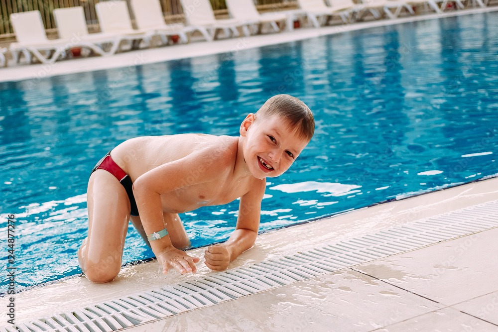 six-year-old boy in swimming shorts gets out of the outdoor pool on vacation