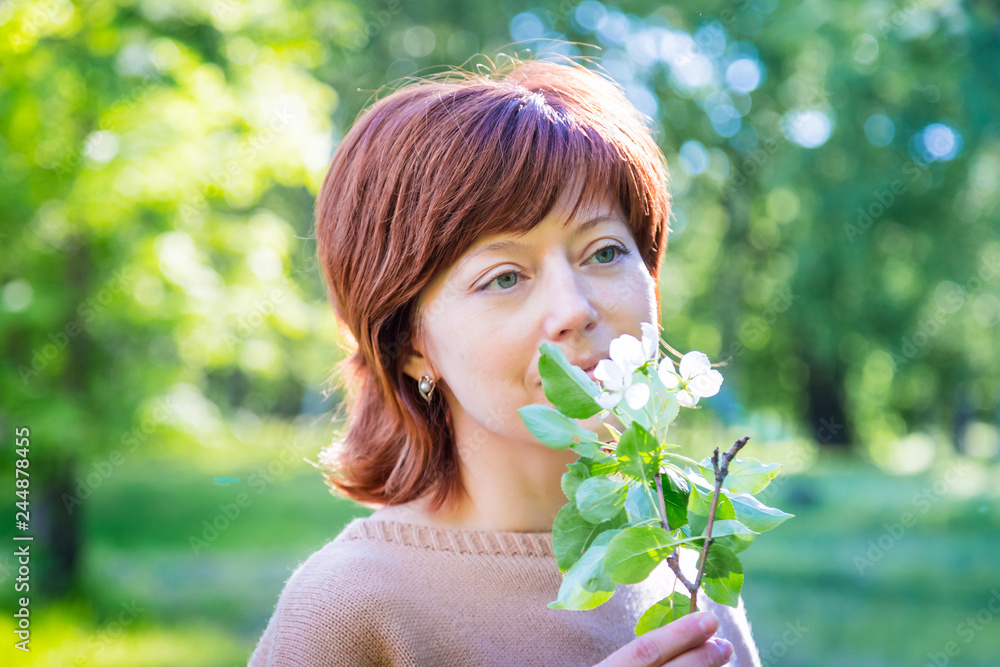 Girl with red hair in the park with blooming apple trees. Portrait of ordinary girl. Harmony concept