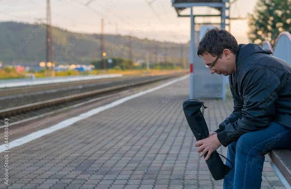 Man sitting on the street on the platform on a bench with a sad face, thinking and waiting for the train