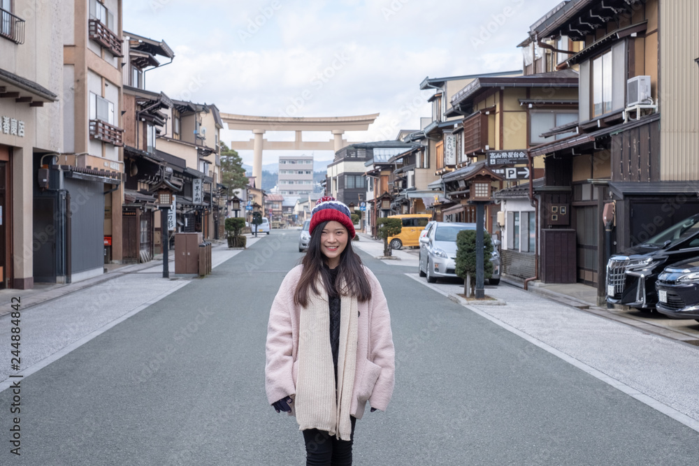 Takayama, Gifu, Japan - December 2018 : Happy Asian Girl with pink overcoat photo in front of giant Torii gate in Hida-Takayama old town, Chubu regional during cold weather in winter.