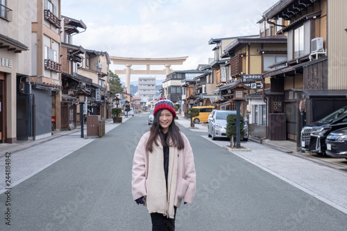 Takayama, Gifu, Japan - December 2018 : Happy Asian Girl with pink overcoat photo in front of giant Torii gate in Hida-Takayama old town, Chubu regional during cold weather in winter. © chayakorn