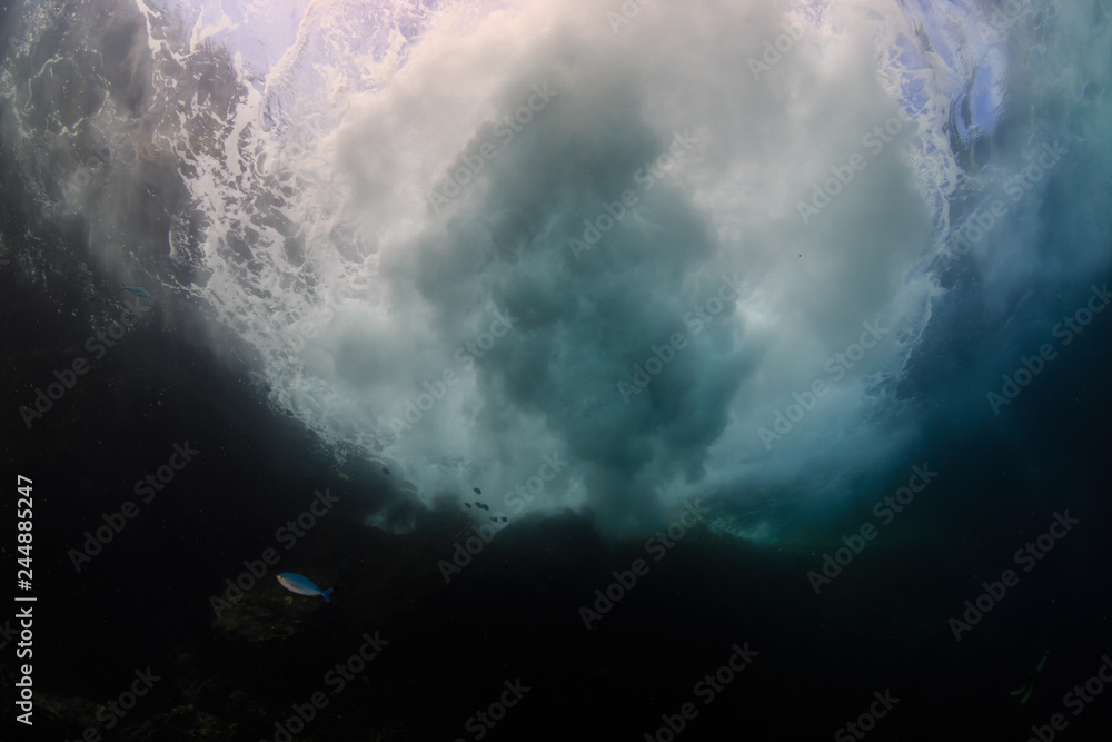 Underwater view of waves crashing against rocks producing bubbles, foam and spray