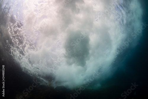 Underwater view of waves crashing against rocks producing bubbles, foam and spray