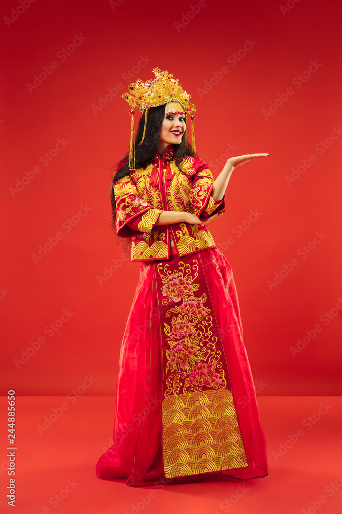 Chinese traditional graceful woman at studio over red background. Beautiful girl wearing national costume. Chinese New Year, elegance, grace, performer, performance, dance, actress, dress concept