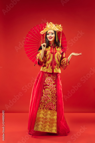Chinese traditional graceful woman at studio over red background. Beautiful girl wearing national costume. Chinese New Year, elegance, grace, performer, performance, dance, actress, emotions concept © master1305