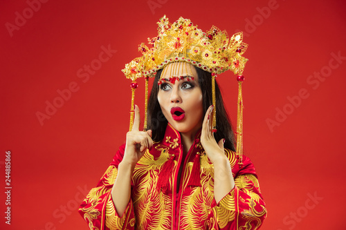 Chinese traditional graceful woman at studio over red background. Beautiful girl wearing national costume. Chinese New Year, elegance, grace, performer, performance, dance, actress, emotions concept