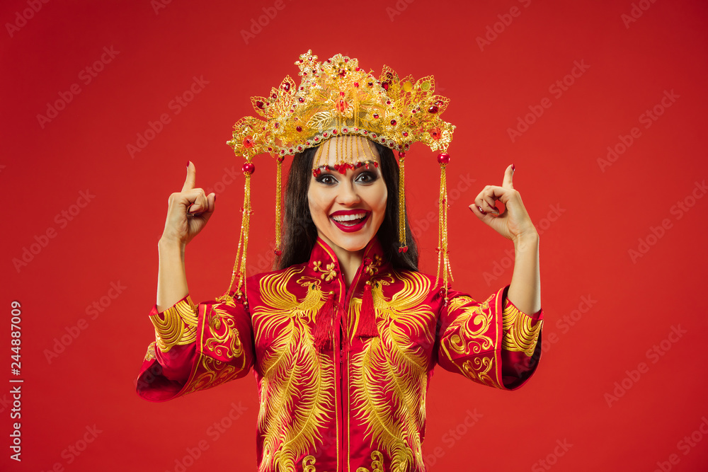 Chinese traditional graceful woman at studio over red background. Beautiful girl wearing national costume. Chinese New Year, elegance, grace, performer, performance, dance, actress, emotions concept