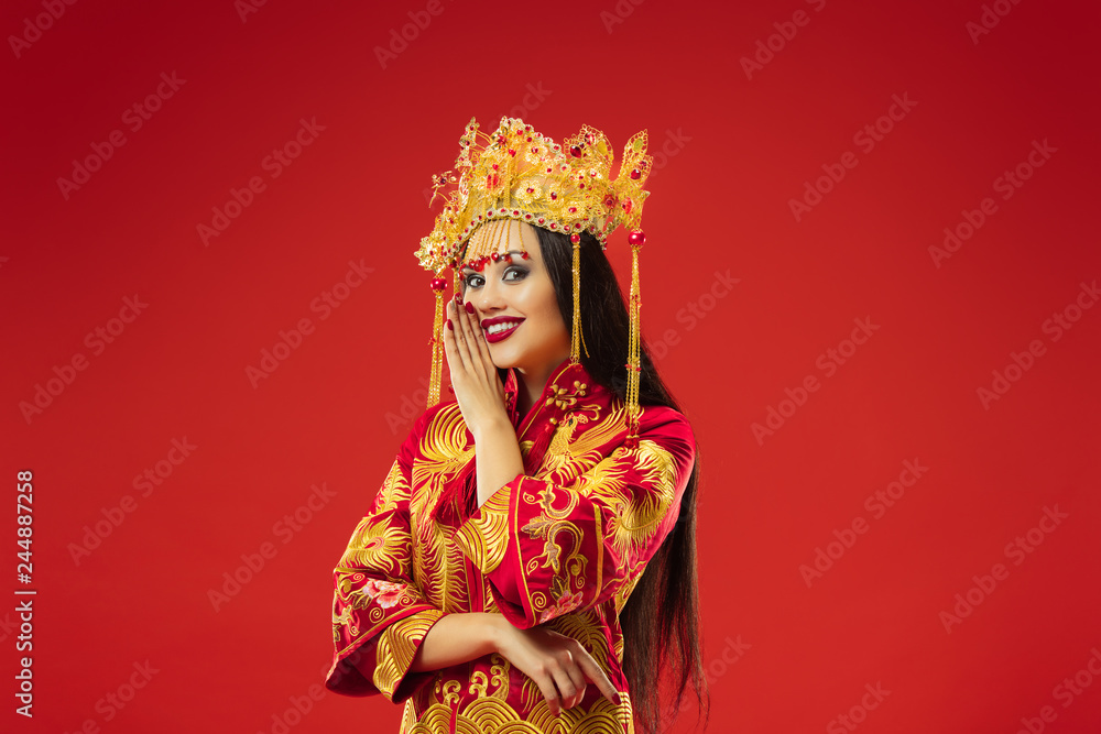 Chinese traditional graceful woman at studio over red background. Beautiful girl wearing national costume. Chinese New Year, elegance, grace, performer, performance, dance, actress, dress concept