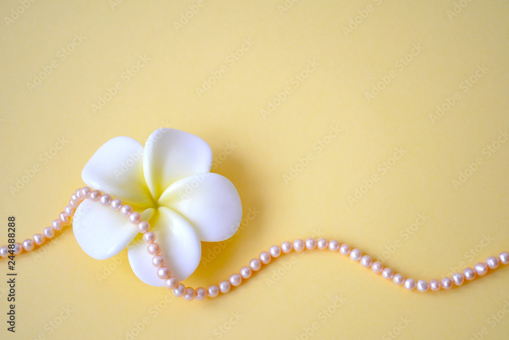 Horizontal background from beads from natural sea pink pearls and a white flower on a yellow background Horizontal background from beads from natural sea pink pearls and a white flower on a yellow background