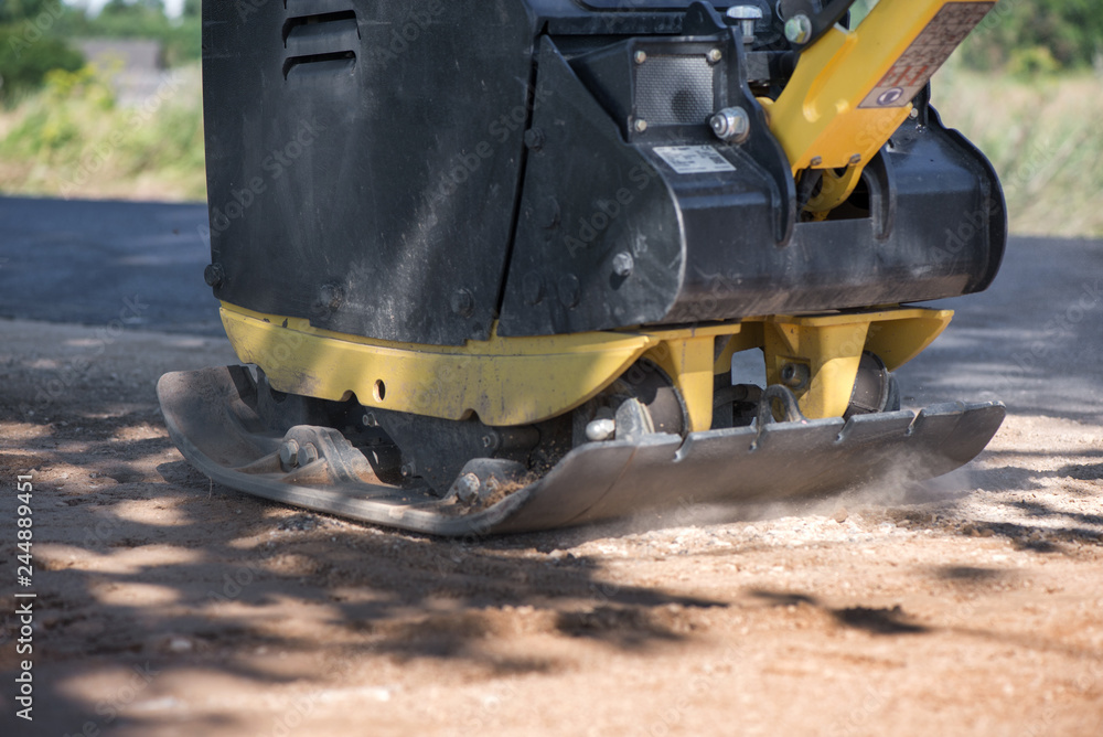 Manual road repair vibrating machine being pushed by a worker during road construction work on gravel road curbs. Road repairing in city. Heavy machinery Manual road repair vibrating machine being pushed by a worker during road construction work on gravel road curbs. Road repairing in city. Heavy machinery