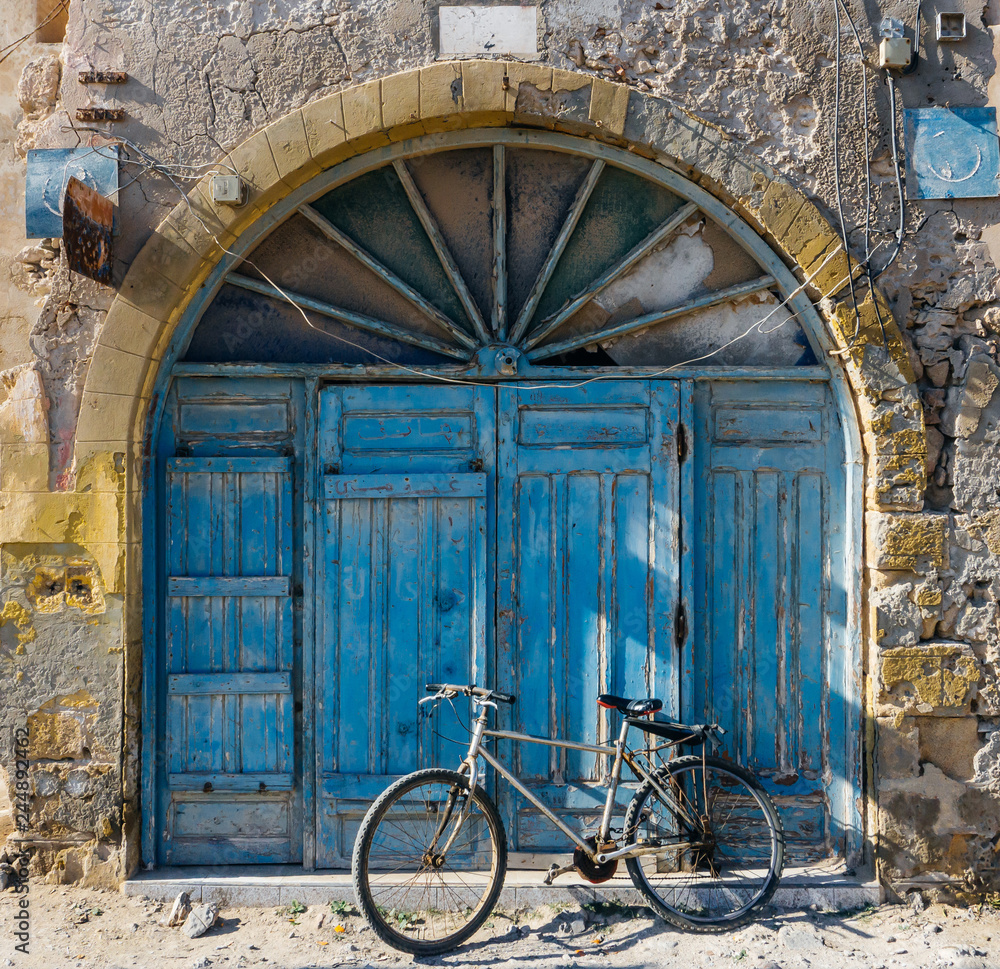 Old blue wrabic door in Morocco (Marrakesh) and bicycle. Traditional oriental style and design in Muslim countries