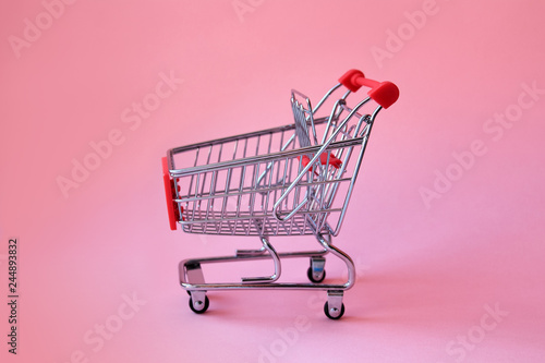 Shopping trolley on soft pink pastel background with copy space. Shopping cart on pink background in minimalism style.