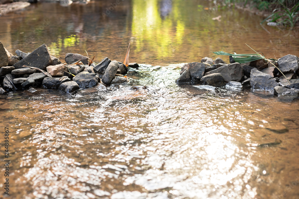 Fototapeta premium weir in river made from natural stone with people reflection on top