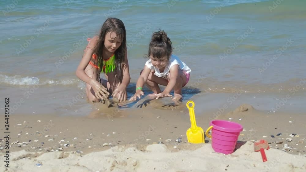 Children playing with sand on the seaside. Happy little girls play with sand on the beach by the sea. Children playing with sand on the seaside. Happy little girls play with sand on the beach by the sea.