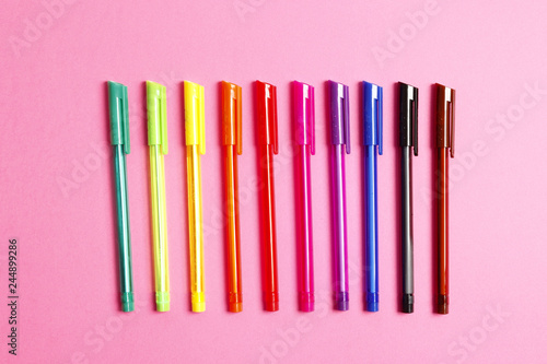 Set of multicolored pens on a pink background. Place for text. Top view.