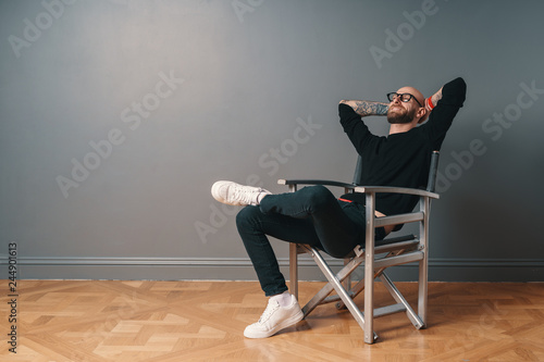 Modern man sitting on couch with laptop relaxing with hands behind head