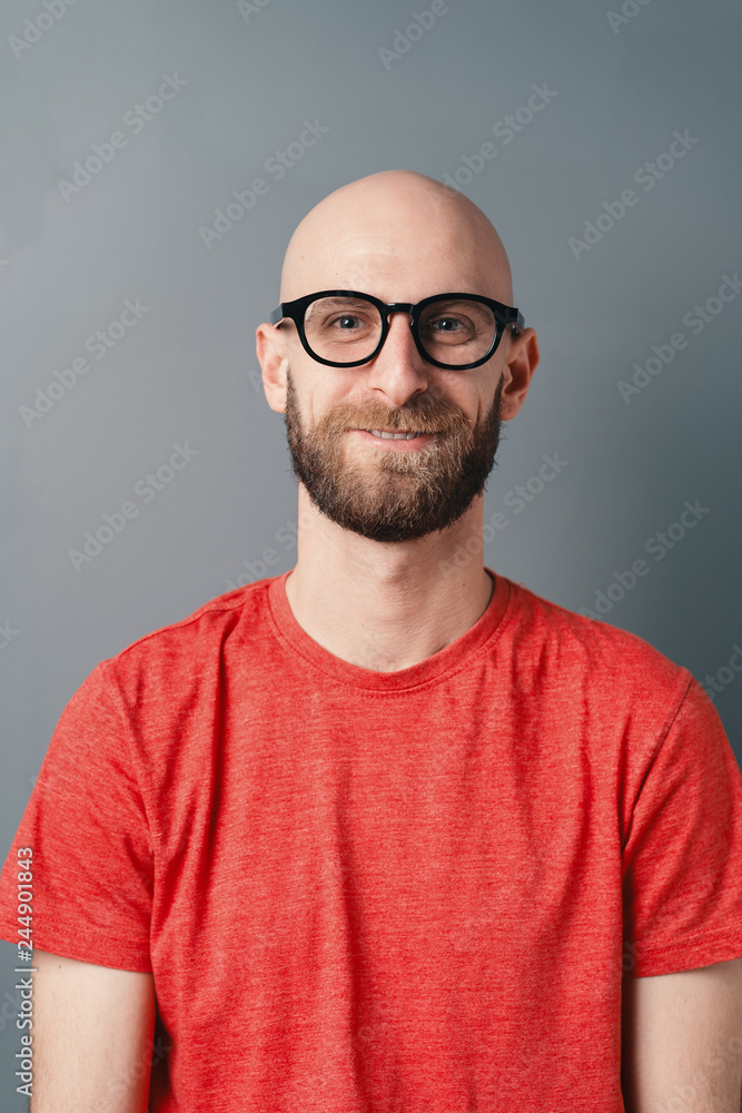 Young smiling man close-up portrait with beard and glasses on gray studio background Young smiling man close-up portrait with beard and glasses on gray studio background