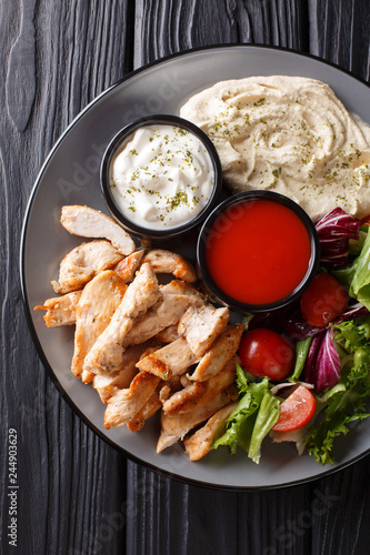 Healthy shawarma plate with chicken, hummus, salad and sauces close-up on a table. Vertical top view