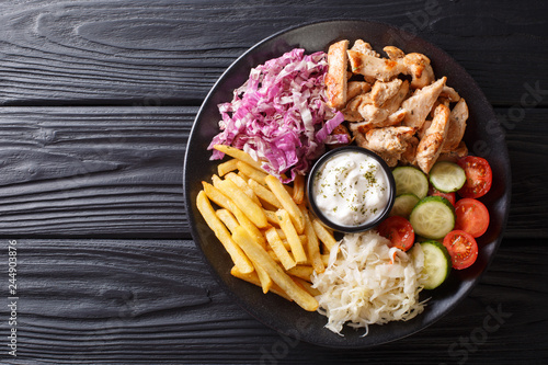 Doner kebab on a plate with french fries, salad and sauce close-up on a table. Horizontal top view