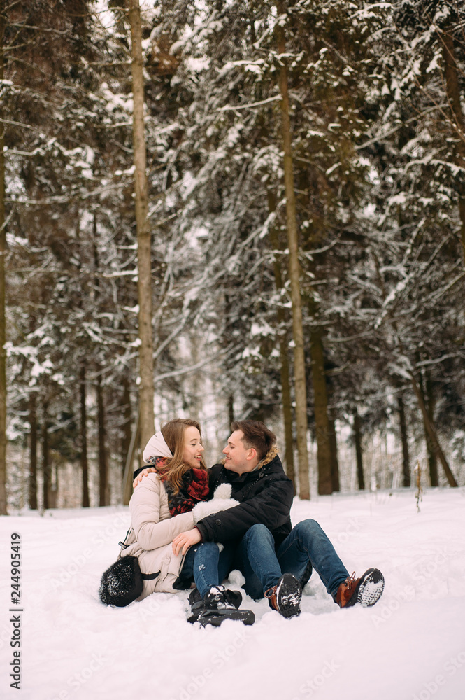 young couple having fun in winter park with their dog. Hugging young couple in love walking with dog outdoors in snowy winter